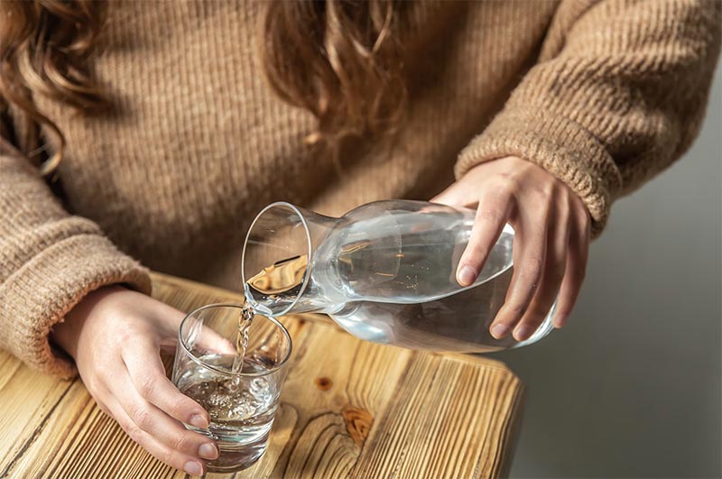 woman pours water into a glass from a glass decanter